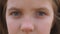 Close up blue eyes of unhappy little blonde girl blinking and looking into camera with a despairing sight. Sorrowful