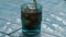 Close up of blue glass with sparkling cola with ice cubes beverage standing on blue table with water. Coke soda pouring