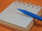 Close-up of a blue mechanical pencil and a small blank notepad