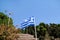 Close up of blue and white Greek flag on flagpole flying in the wind. Torn Greek national flag on old construction waving.