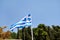 Close up of blue and white Greek flag on flagpole flying in the wind. Torn Greek national flag on old construction waving.