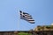 Close up of blue and white Greek flag on flagpole flying in the wind. Torn Greek national flag on old construction waving.