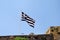 Close up of blue and white Greek flag on flagpole flying in the wind. Torn Greek national flag on old construction waving.