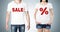 Close up of the bodies of man and woman in a white t-shirts with the red percentage sign and the word \' sale \' on the chest.