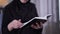 Close-up of book in female Muslim hands. Blurred woman in traditional black hijab reading at the background. Lifestyle