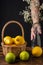 Close-up of bottle with flowers and woman`s hand holding it, basket with lemons, on wooden table, black background
