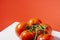 Close-up of a bouquet of five wet red natural tomatoes on a white table and a red background