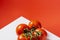 Close-up of a bouquet of four wet red natural tomatoes on a white table and a red background