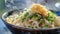 A close up of a bowl of steaming hot udon noodles adorned with scallions and tempura flakes at a Japanese food festival