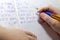 Close-up of boy hand with pencil writing english words by hand on traditional white notepad paper.