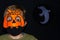 Close up Boy in orange pumpkin and medical mask.Moon reflector with ghost silhouette on dark background