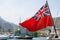 Close-up of the British Red Ensign aboard a ship with ships and mountains in the background. Red flag with the first