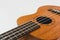 Close up of brown Ukulele on white background. Ukulele strings, saddle, soundhole, ukulele body, neck, fretboard.