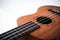 Close up of brown Ukulele on white background. Ukulele strings, saddle, soundhole, ukulele body, neck, fretboard.