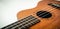 Close up of brown Ukulele on white background. Ukulele strings, saddle, soundhole, ukulele body, neck, fretboard.