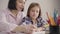 Close-up of brunette caucasian woman sitting with daughter at the table and dictating. Wise parent helping schoolgirl