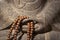 Close up on a Buddha statue hands holding a wooden prayer beads rosary