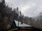 Close up of building roof with chimney in mountainous terrain. Smoke billows from smokestack into surrounding atmosphere