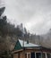 Close up of building roof with chimney in mountainous terrain. Smoke billows from smokestack into surrounding atmosphere