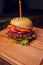 Close Up of Burger Piled High with Fresh Toppings on Whole Grain Artisan Bun, on Rustic Wooden Surface with Dark