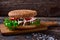 Close Up of Burger Piled High with Fresh Toppings on Whole Grain Artisan Bun, on Rustic Wooden Surface with Dark Background and Co