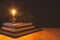 Close-up of burning candle with pile of old book on wooden table