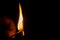 Close-up of a burning matchstick held in a hand on a black background