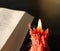 Close up of a burning peach dripping candle with an open Bible