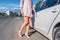 Close-up of a business lady woman, opens the door of a white business sedan, beige formal suit, high-heeled shoes