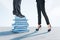 Close up of businessman and businesswoman feets and legs standing on top of stacked books. Light wallpaper. Education, wisdom,