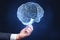 Close up of businessman hand holding glowing human brain hologram on blurry wall background. Neurology research and artificial