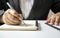 Close-up of a businesswoman using a pen to write a wooden desktop notebook.