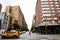 A close up of a busy city street in New York. A pedestrian crossing the street and a yellow taxi on the road.