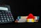 Close up of a calculator, toy home, money bundles shot against black background
