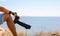 Close-up of a camera in a man`s hand on the edge of a steep cliff over the sea.