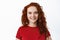 Close-up of candid smiling woman with red curly hair and pale healthy skin, looking cheerful at camera, standing in t