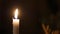 Close-up of candle flame in black background, someone moving behind the candle