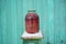 Close up of canned juice with berries on chair with snow on background of old green wooden house. Sealed jar of compote