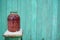 Close up of canned juice with berries on chair with snow on background of old green wooden house. Sealed jar of compote