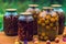 Close up of canned juice with fruits and berries on table in garden. Sealed jars of compote with apricots and flowers on