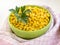 Close-up of canned sweet corn in a green bowl near checkered kitchen towel. Garnish and ingredient for salads. Vegetarian