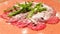 Close up of carpaccio meat with parmesan and arugula in a ceramic large orange plate on a wooden table. With olive oil