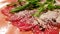 Close up of carpaccio meat with parmesan and arugula in a ceramic large orange plate on a wooden table. With olive oil