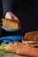 Close-up of carrots, woman`s hand depositing portion on wooden table and carrot cake, with black background