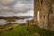 Close up of Castle Tarbert on the right, green grass and rocks in the foreground and tarbert bay in the background with beautiful