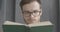 Close-up of Caucasian man in eyeglasses reading book and smiling. Slowmo face of intelligent young reader enjoying