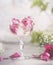 Close up of champagne glass with drink and pink rose petal ice cubes on table with flowers. Romantic table setting for wedding or