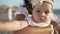 Close-up of charming beautiful baby girl stretching to camera resting in sunlight on Mediterranean sea coast with