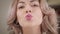 Close-up of charming Caucasian woman applying lipstick, sending air kiss to camera and winking. Happy beautiful girl