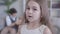 Close-up of charming little brunette girl looking back at blurred boys fighting at the background, shaking head and